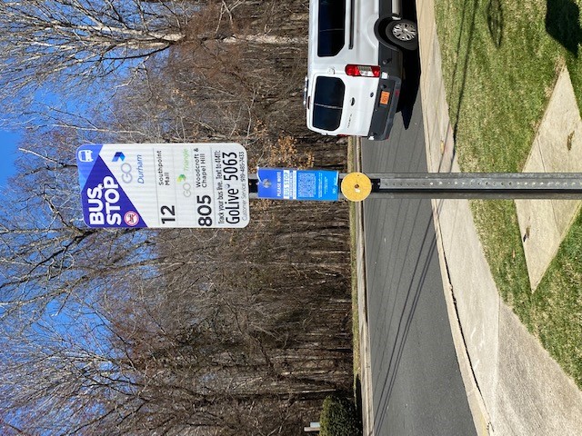 Bus stop sign of NC 54 at Residence Inn Blvd (WB) with improvements card attached