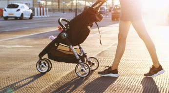 Woman walking with a stroller on a crosswalk with sun rays behind them